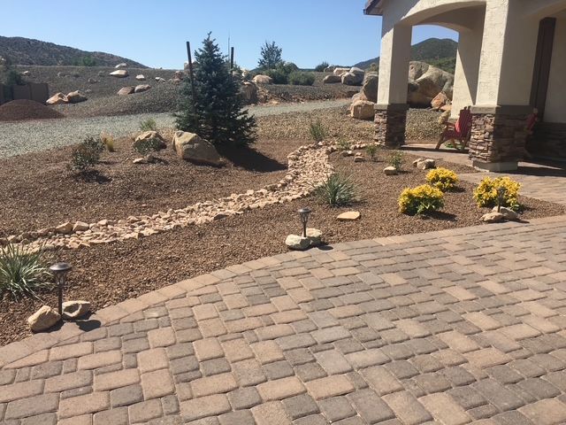 A house with desert landscaping, a brick driveway, and stone-covered landscape. Sunny day.