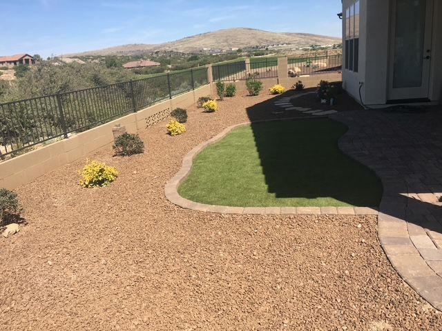 A landscaped yard with a small green lawn, rock ground cover, and bushes, with a mountain in the background.