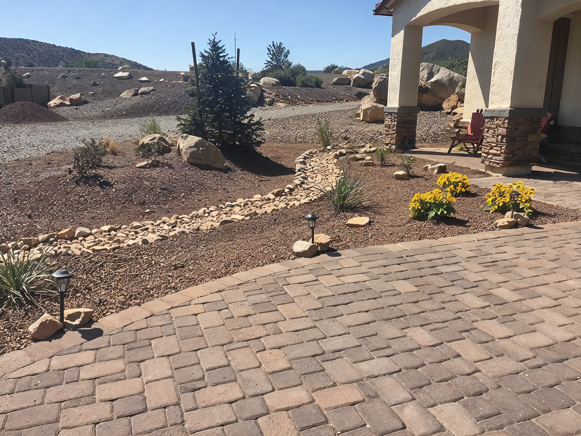 Brick patio leads to a house with a desert landscape and a rock creek bed.