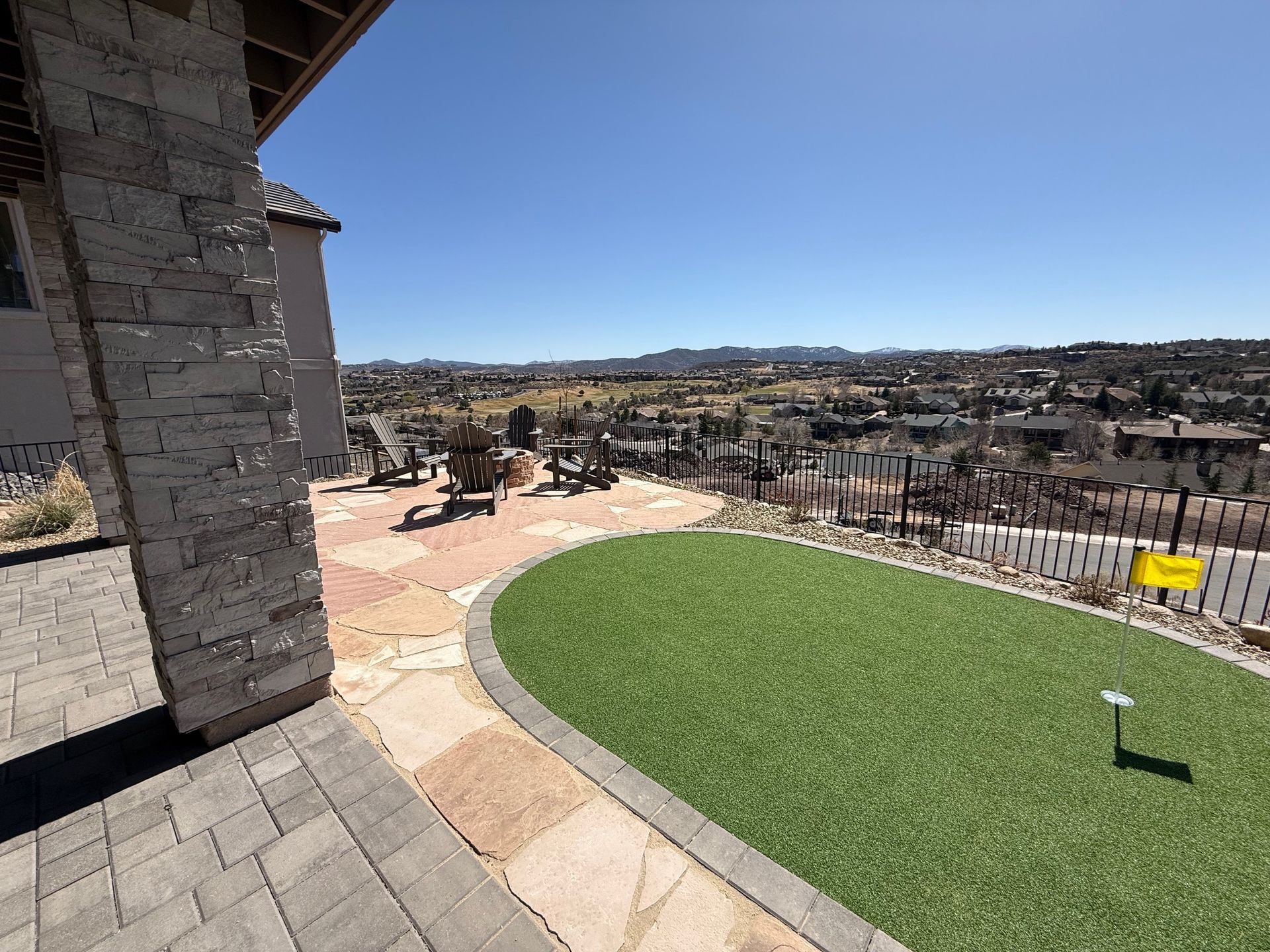 Backyard with artificial turf, stone patio, and distant city views on a sunny day.