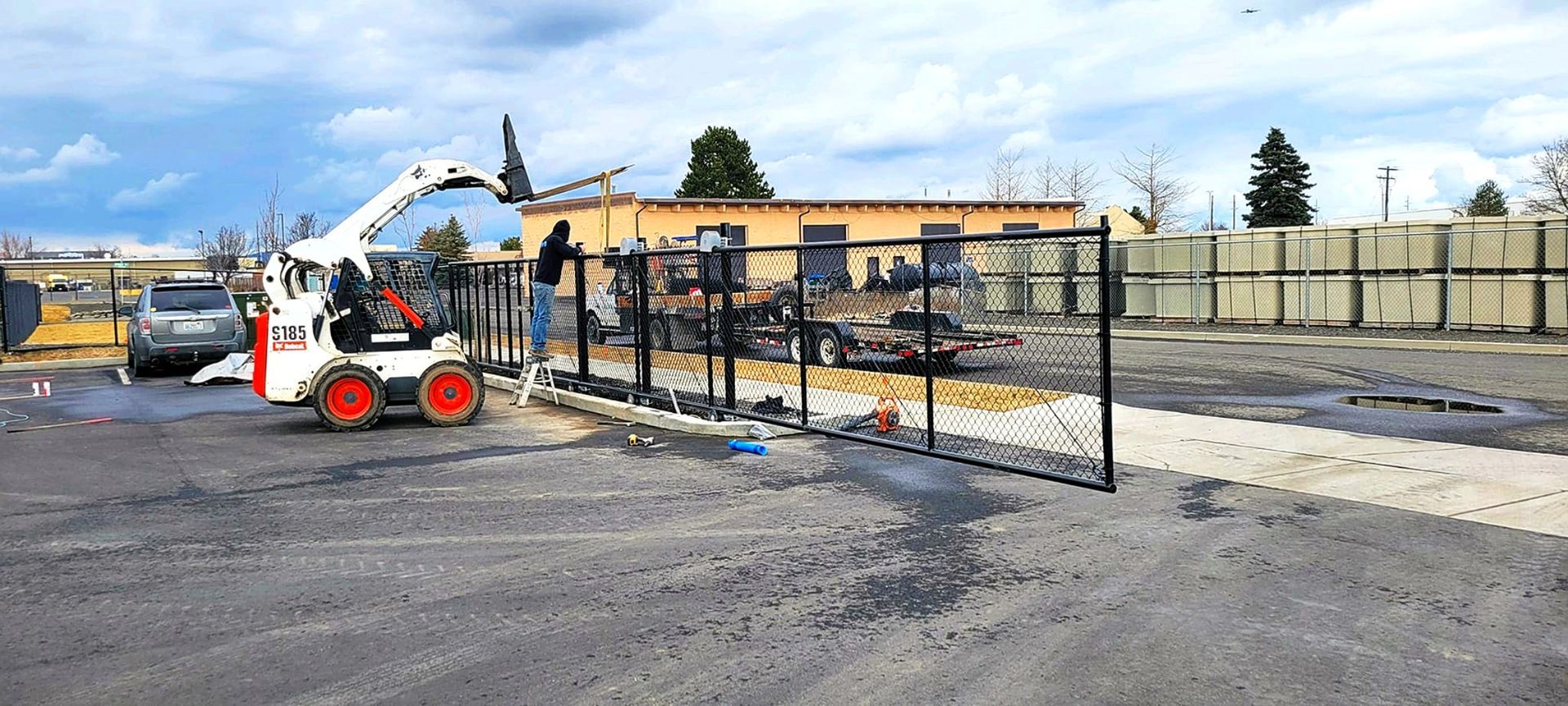 A Bobcat and a person are installing a fence on a construction site.