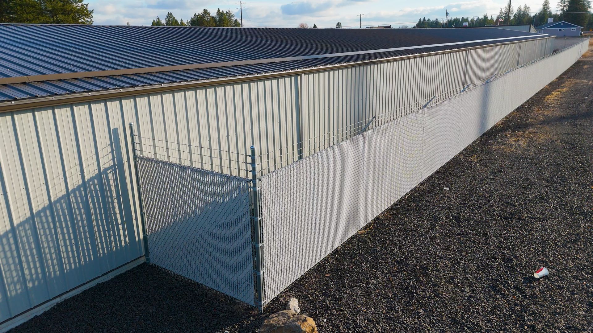 Long fence with white privacy screening next to a gravel path, under a blue sky.
