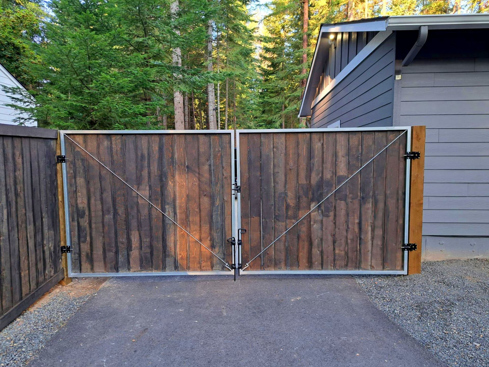 Wooden gates with metal frames, set on a driveway; a house and trees are in the background.