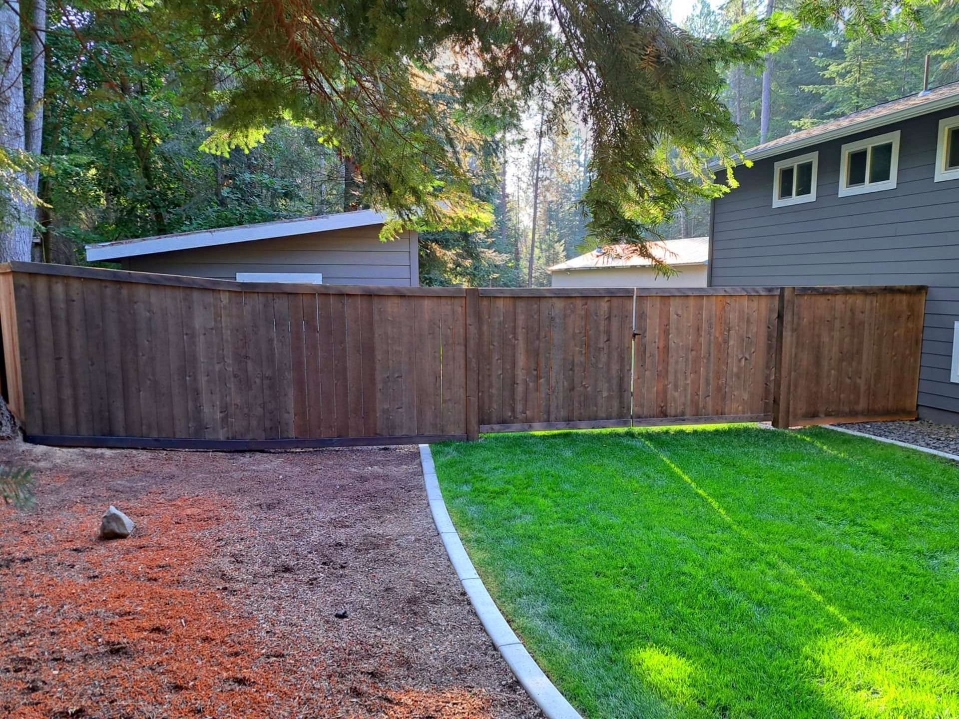 Wooden fence surrounding a backyard with green grass and a house.