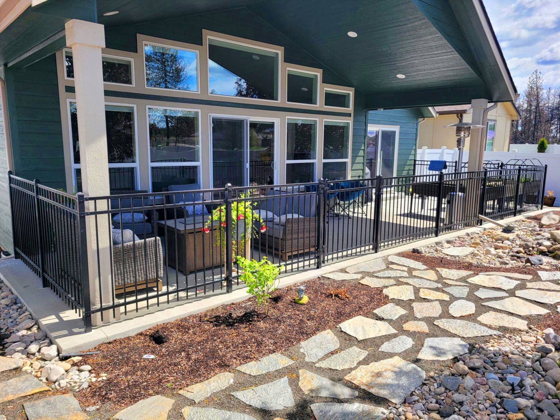 Patio with black metal railing, seating, and flagstone path. Turquoise building and dark mulch.