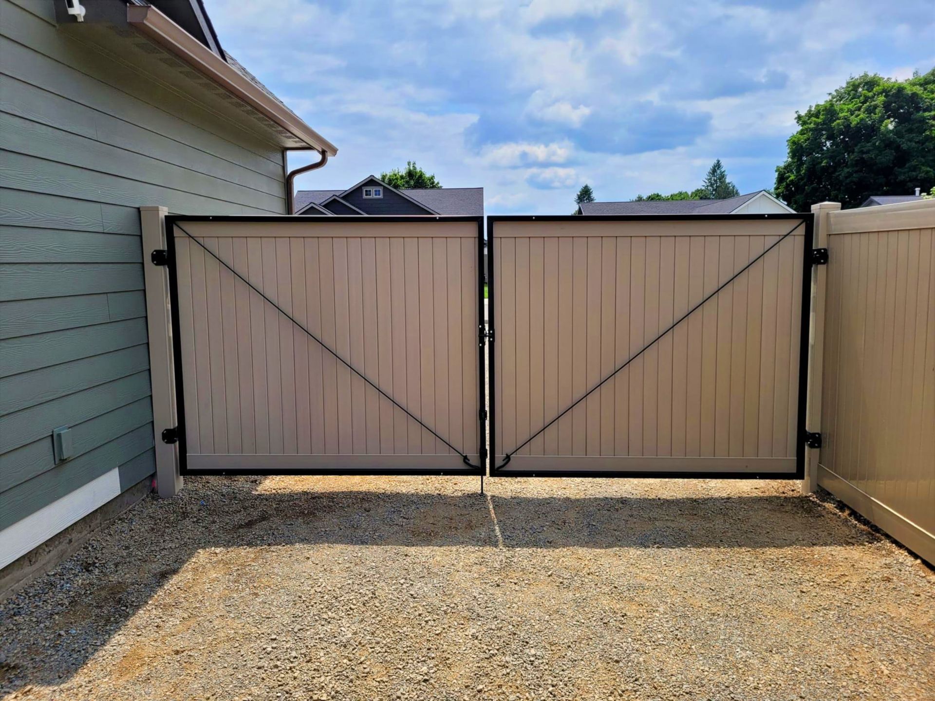 Two tan wooden gates with black metal diagonal braces and border. Set in gravel.