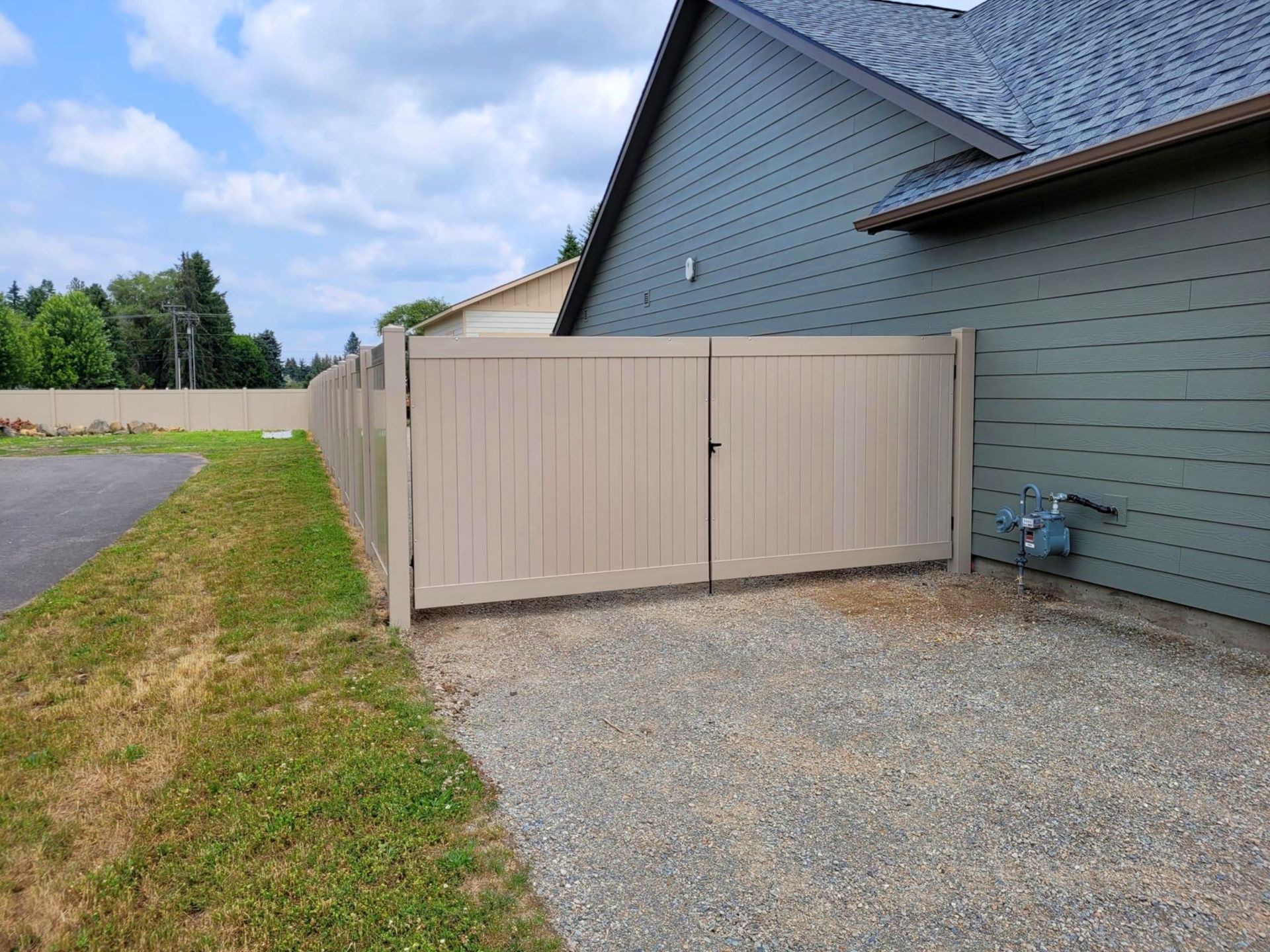Tan vinyl gate next to a house with gravel driveway and green grass.