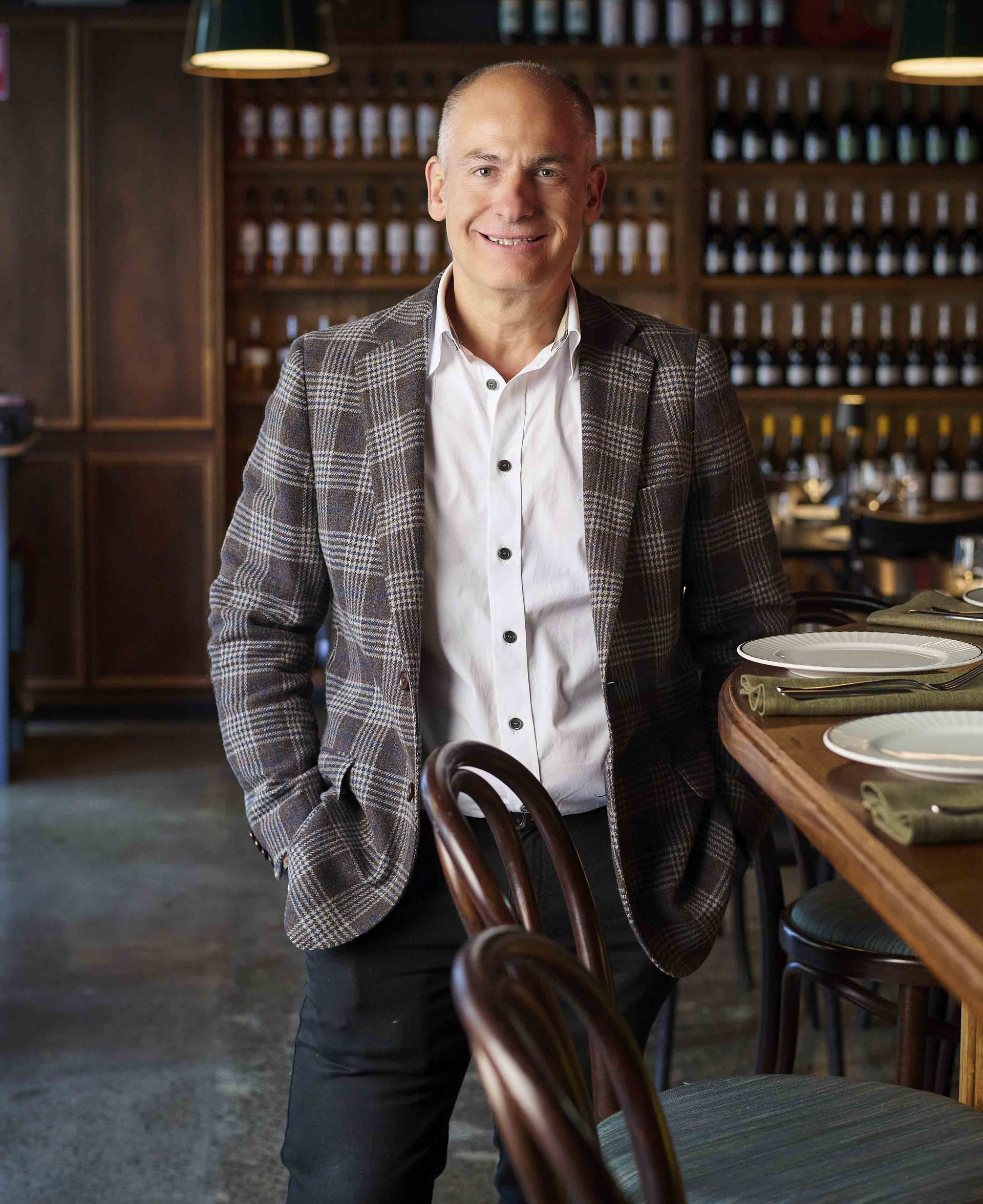 Man in patterned jacket smiles by a restaurant bar.