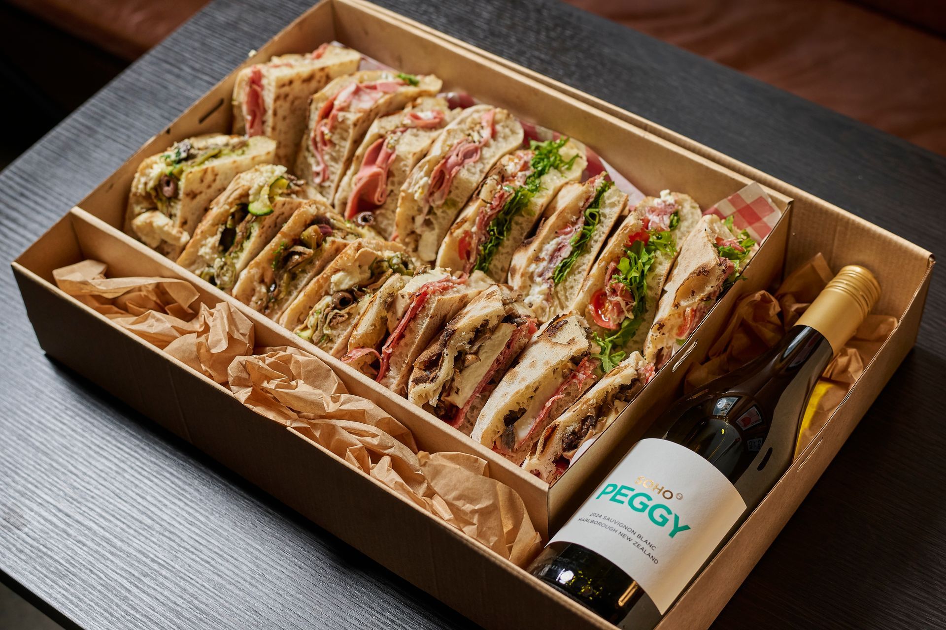 Sandwiches and wine in a box, ready to eat. Brown sandwiches with various fillings, bottle of wine on the side.