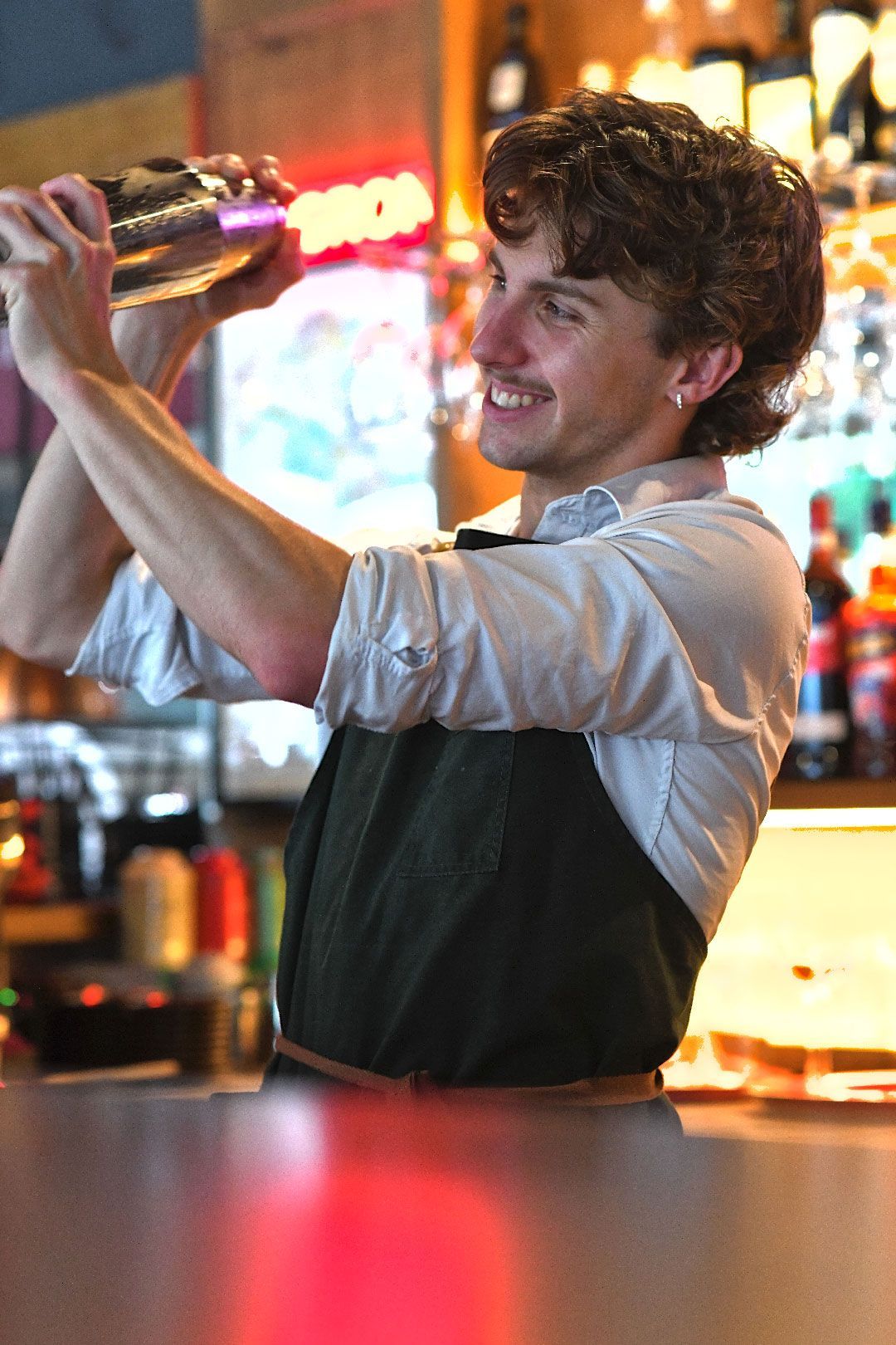 Bartender smiles while shaking a cocktail shaker behind a bar.