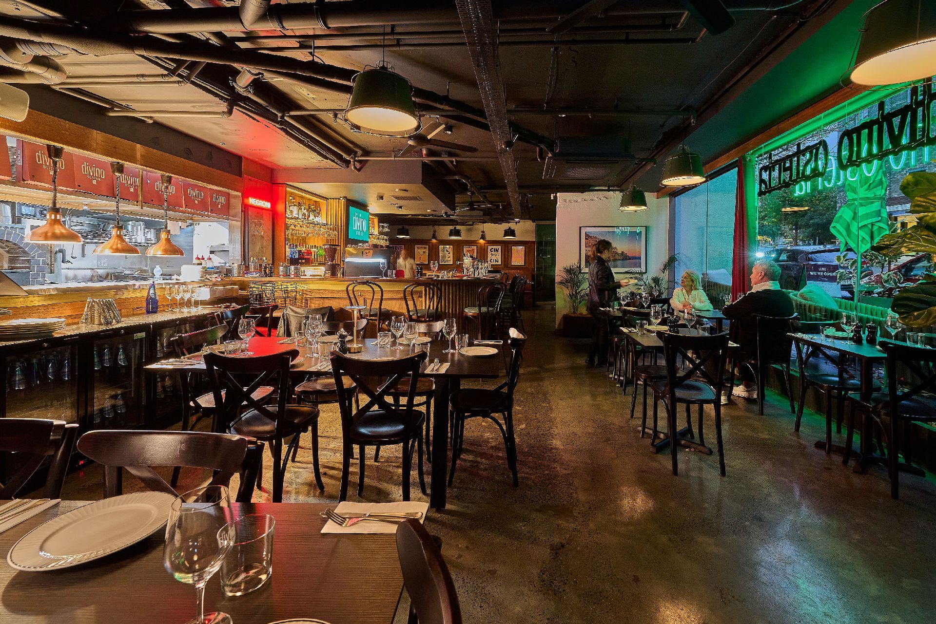 Interior of a restaurant with tables, chairs, bar, and open kitchen. Dim lighting.