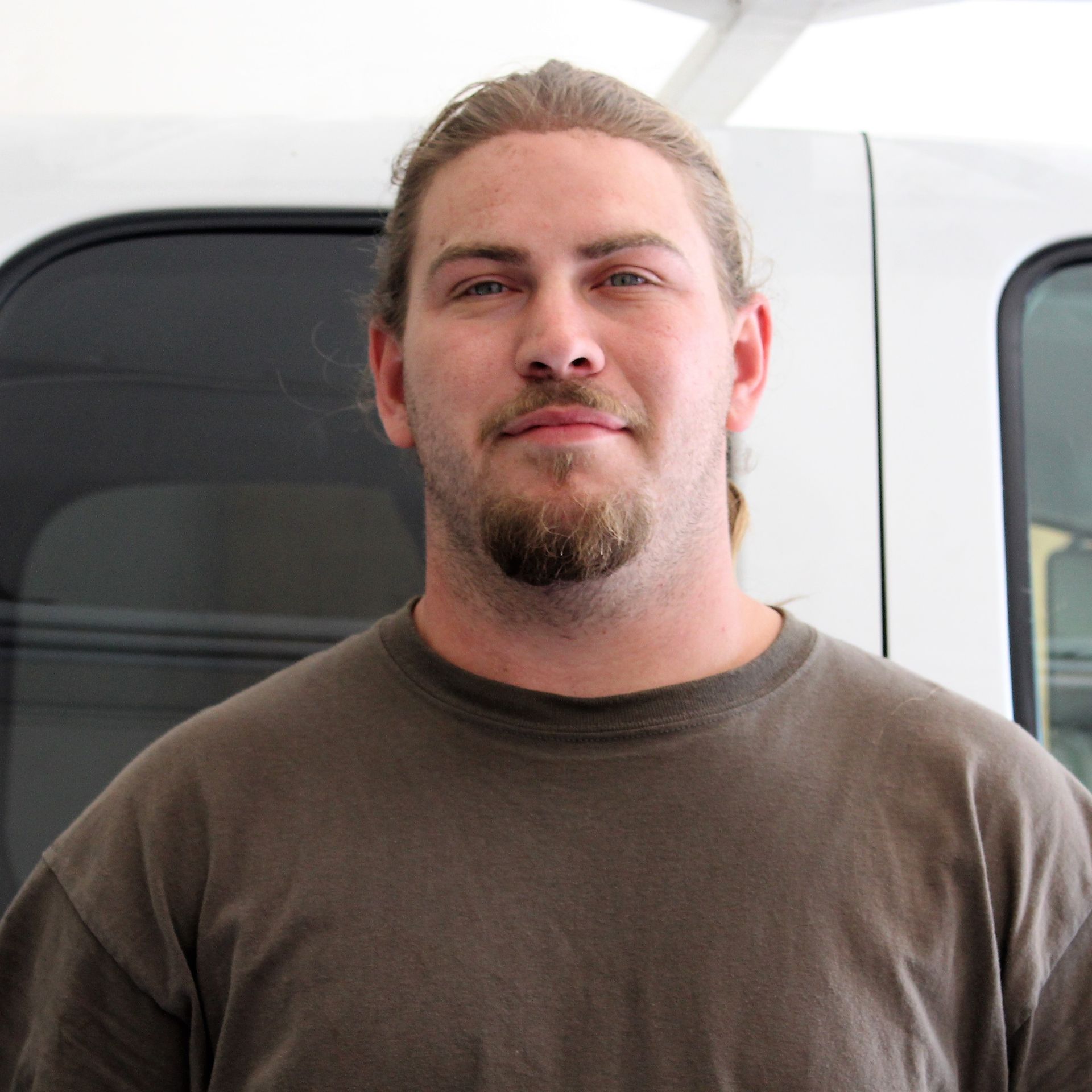 A man with a beard is standing in front of a white van.