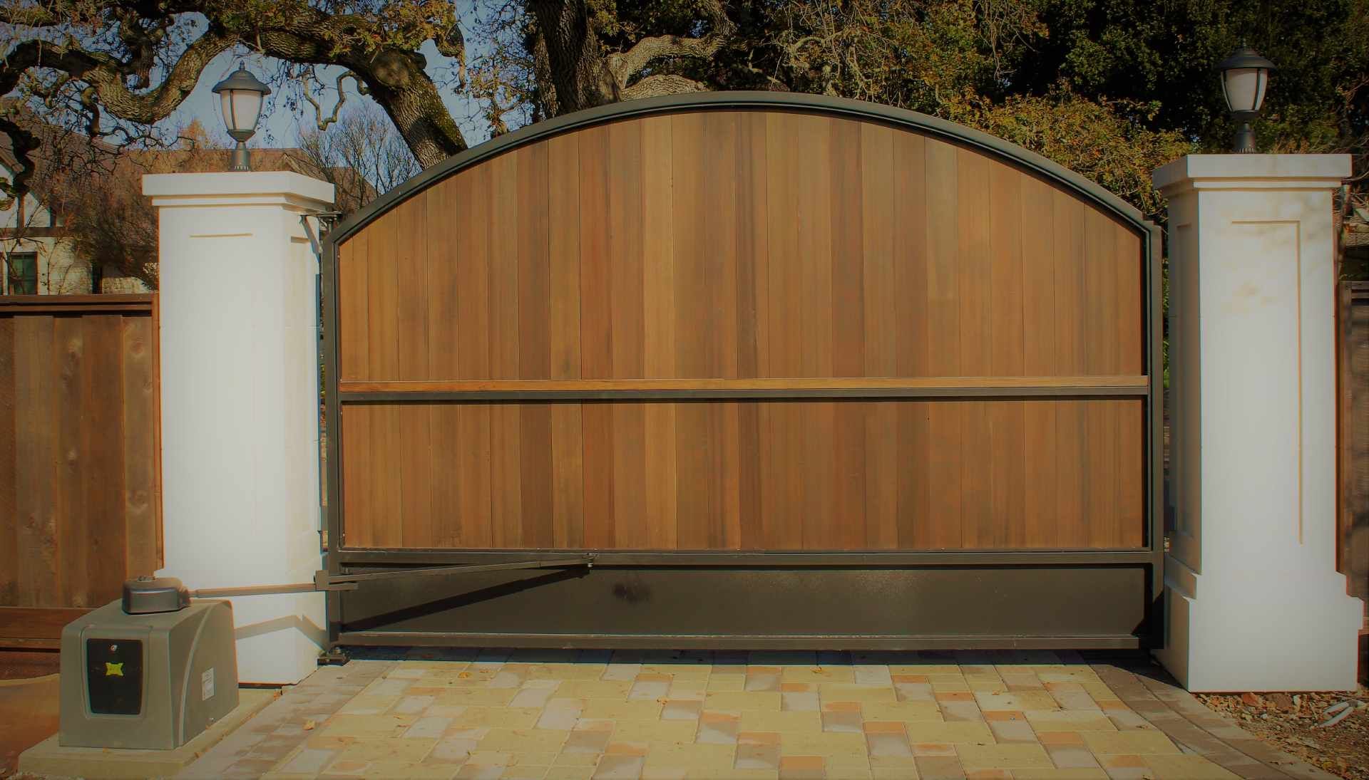 A wooden gate is sitting on a brick driveway next to two white pillars.