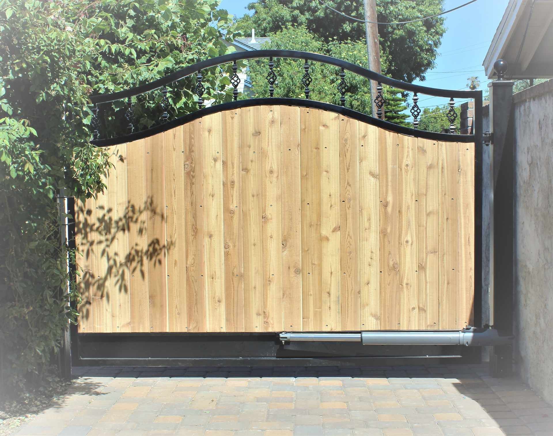A wooden gate with a black frame is open to a driveway