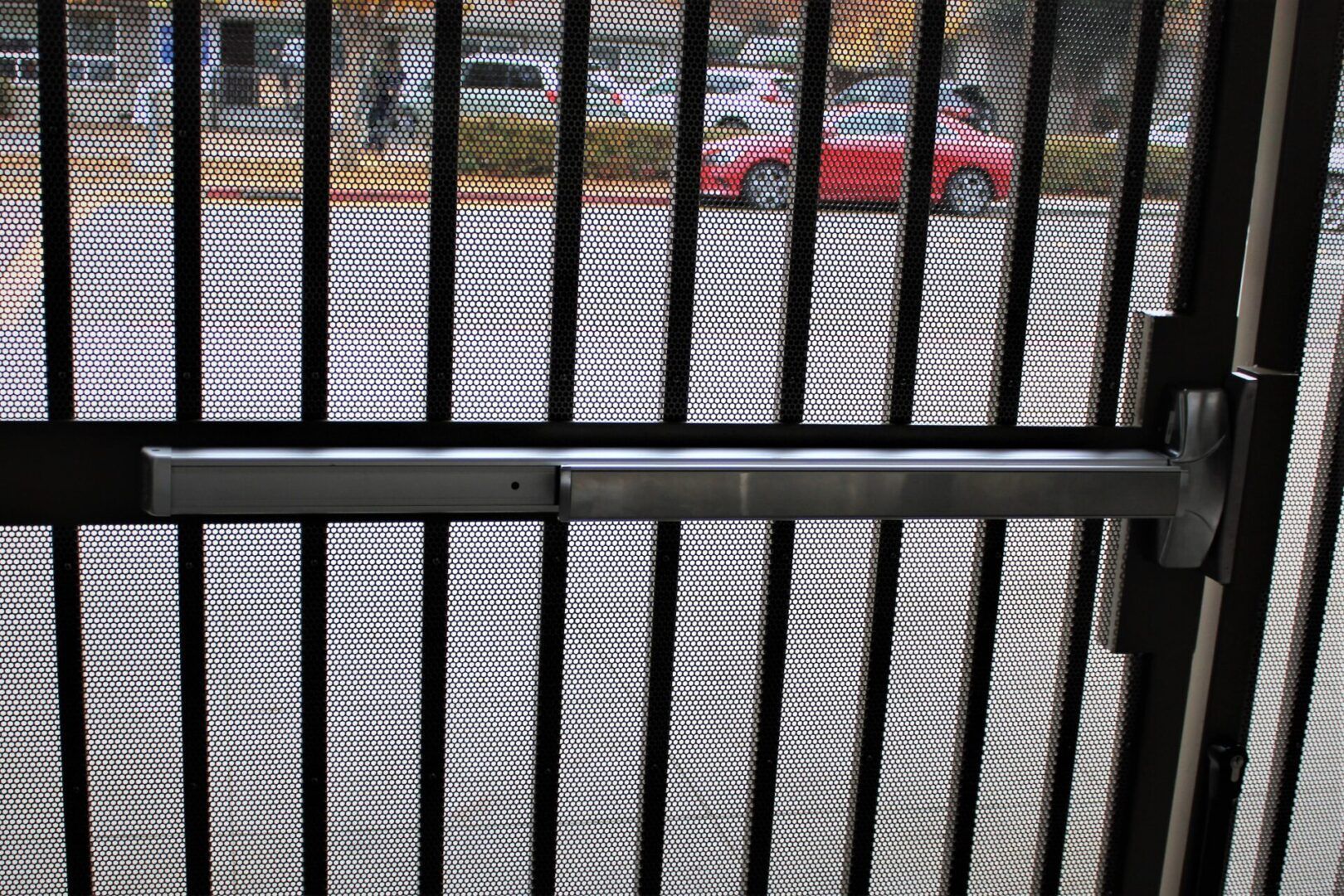 A red car is parked in a parking lot behind a fence.