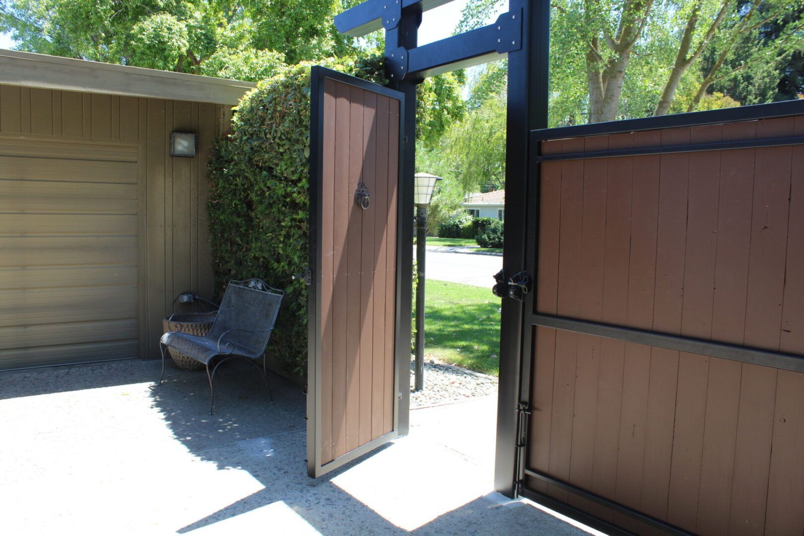 A wooden gate is open to a driveway next to a garage.