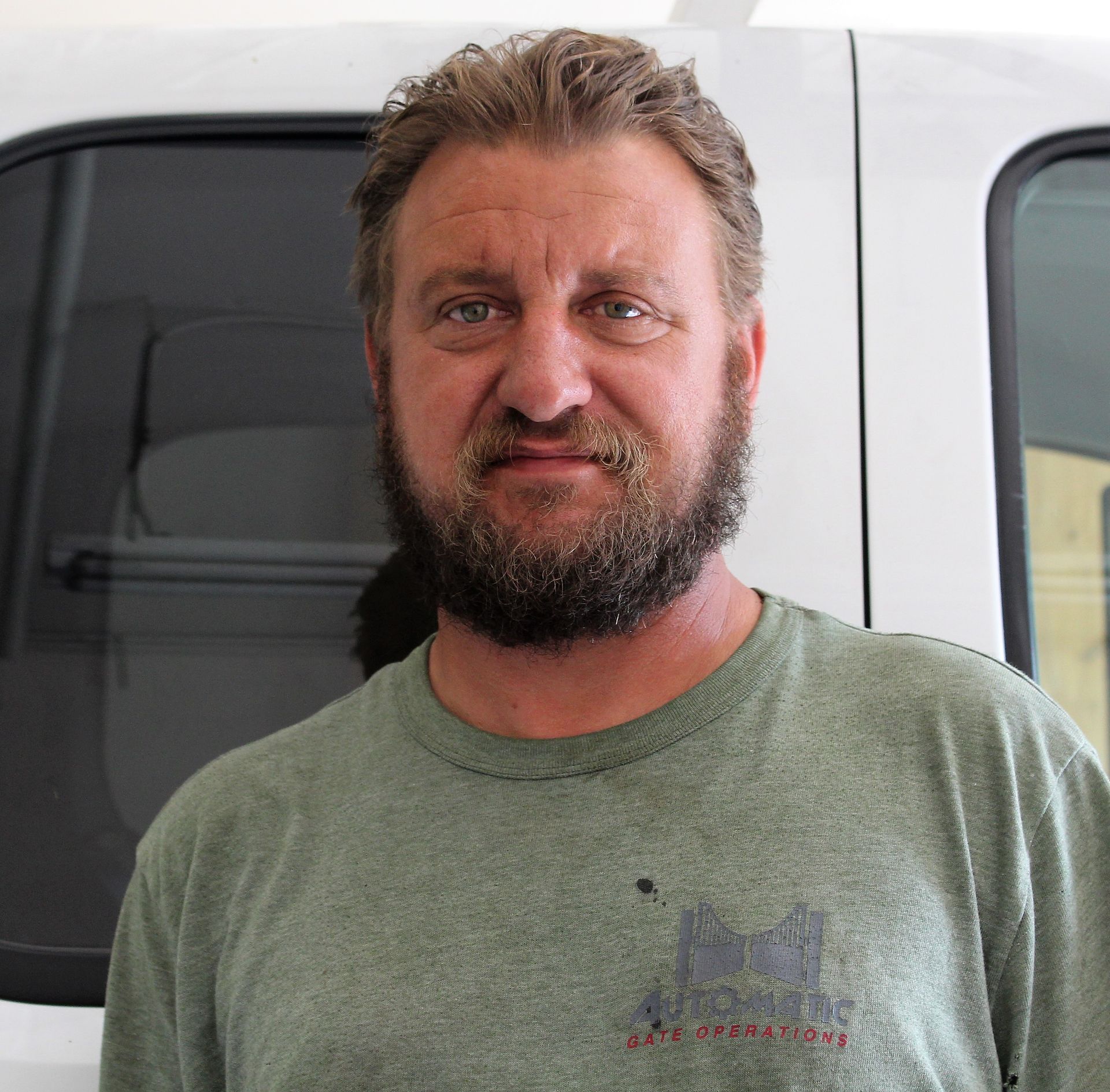 A man with a beard is standing in front of a white van.