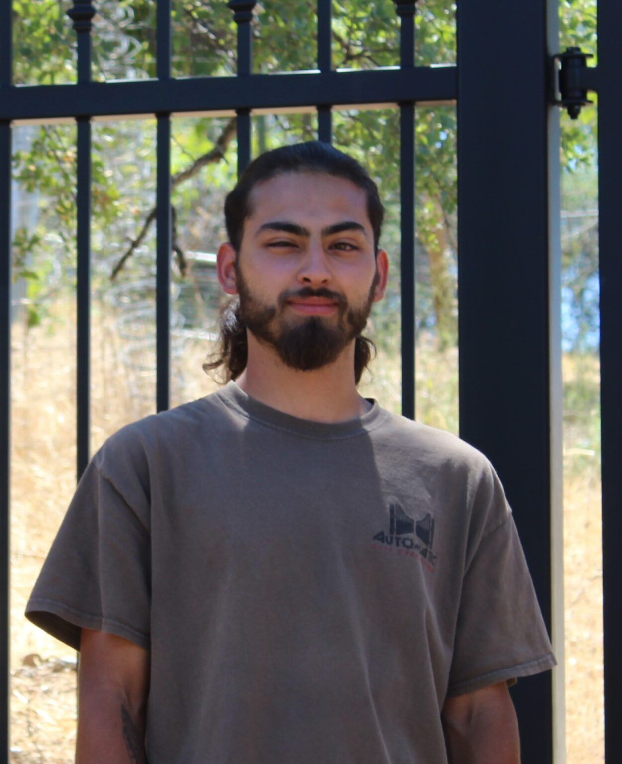 A man with a beard is standing in front of a fence