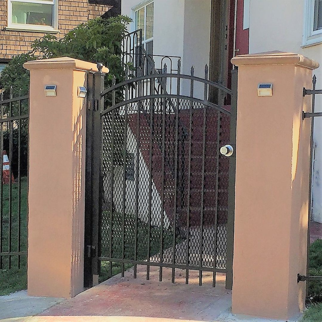 A wrought iron gate is between two pillars in front of a house.
