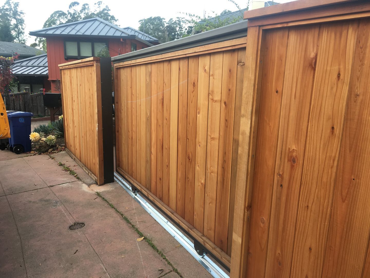 A wooden fence with a sliding gate in front of a house.