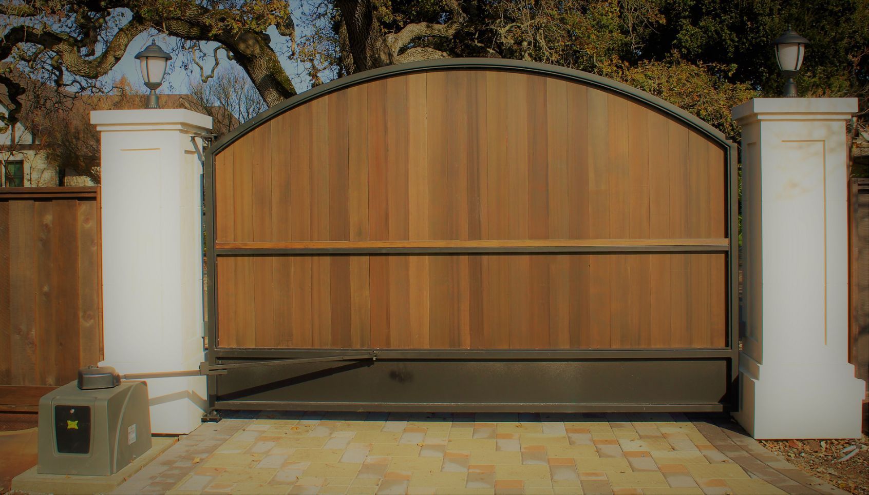 A wooden gate with a metal frame is sitting on a brick driveway.