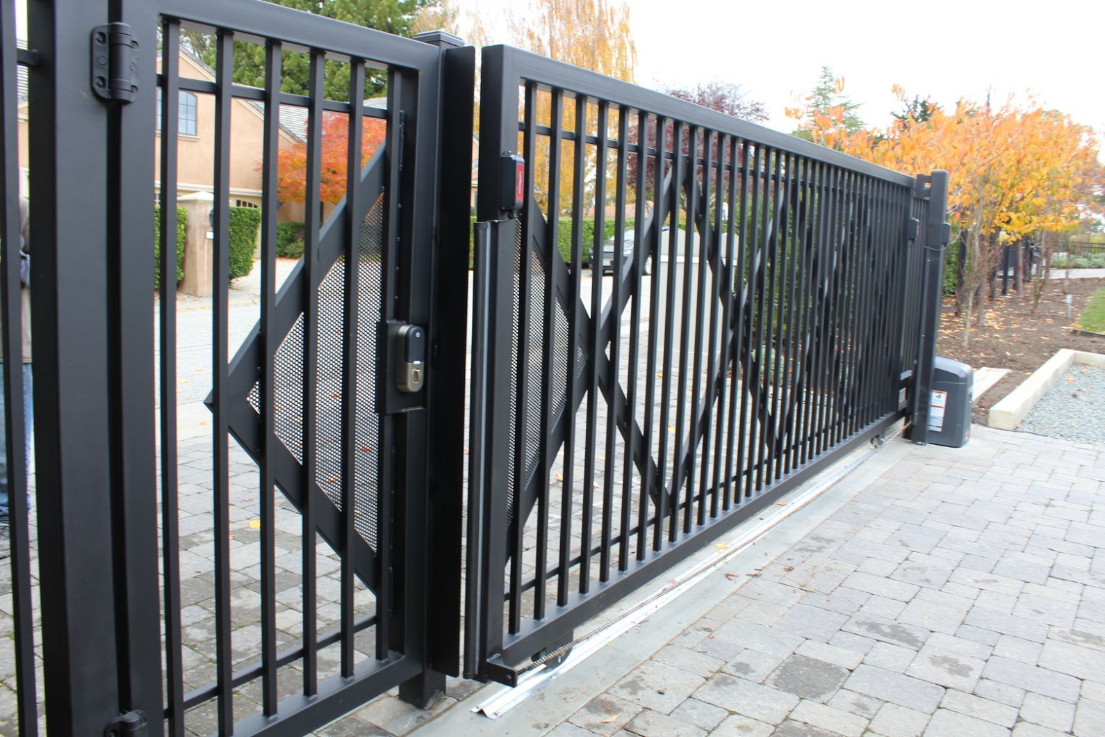 A black sliding gate is open on a brick driveway.