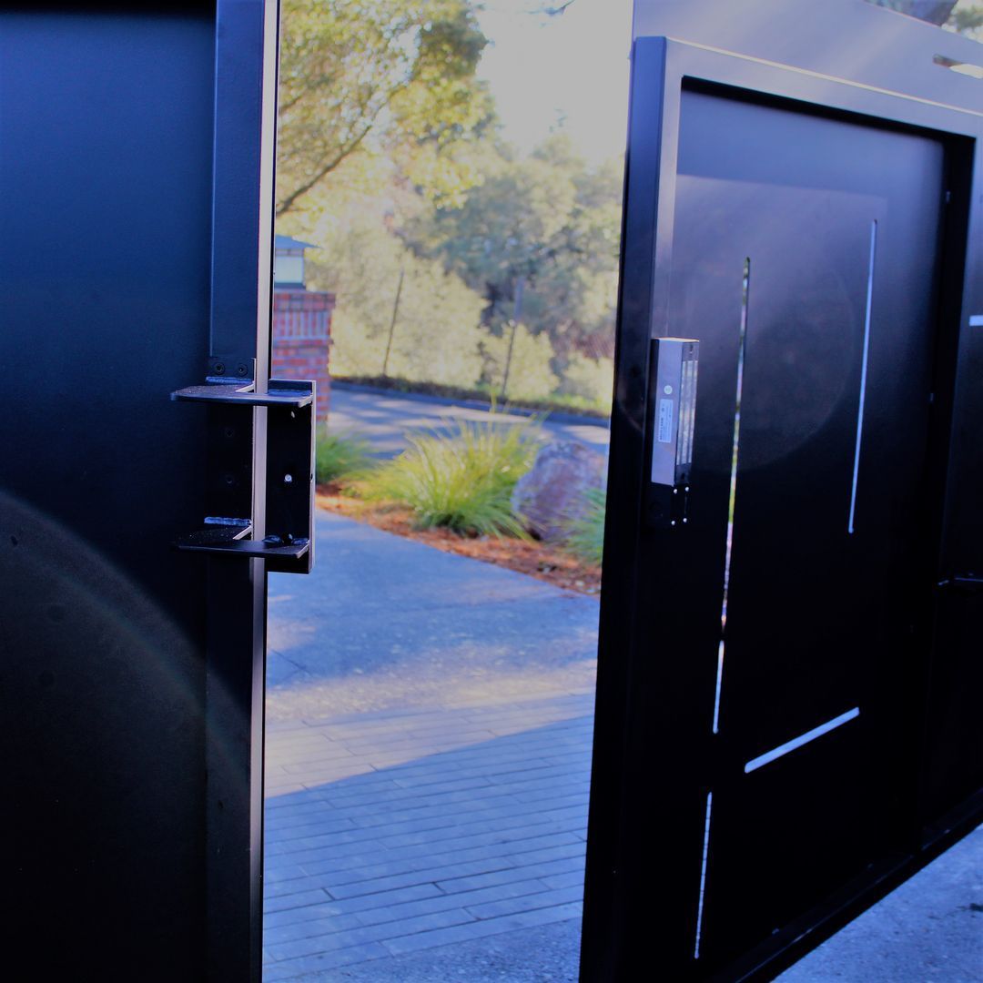 A black gate is open to a driveway with trees in the background.