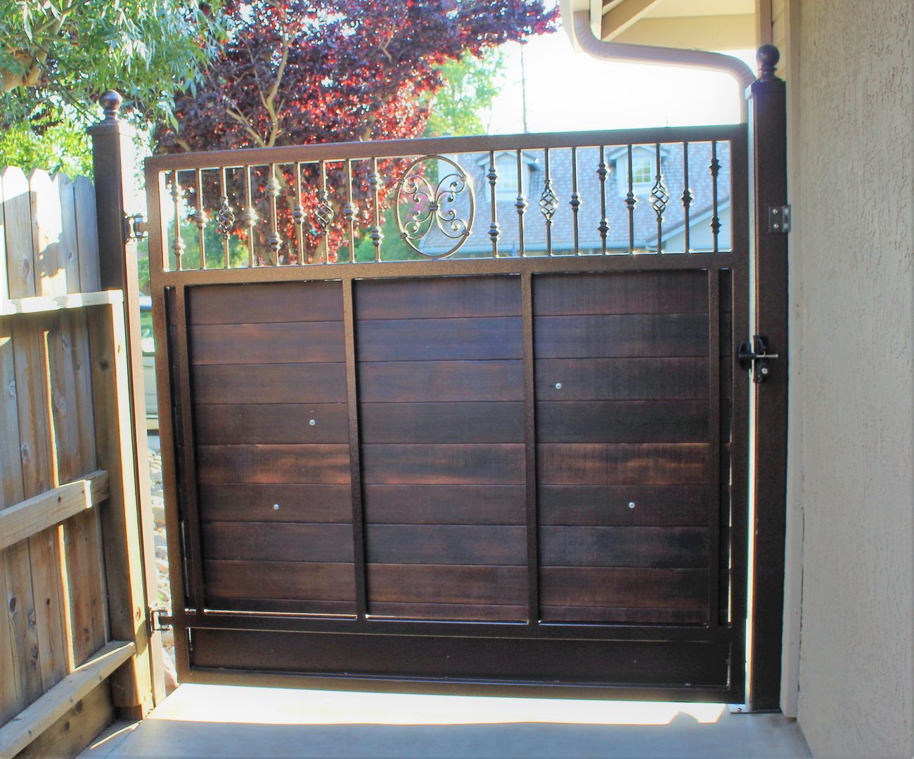 A wooden gate with a metal frame is open to a driveway