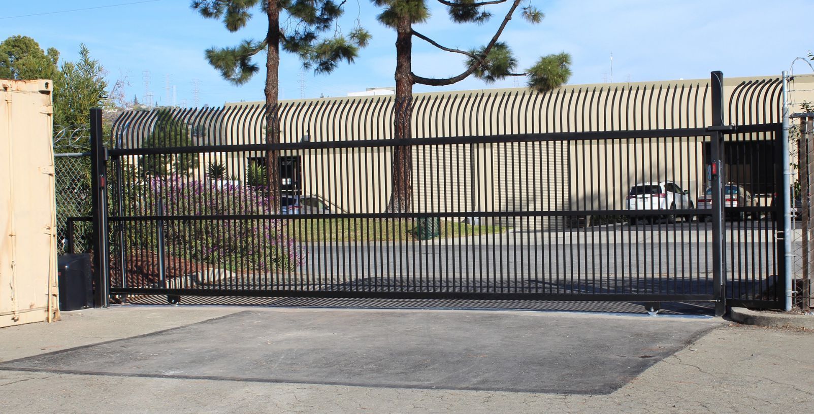 A sliding gate is open to a parking lot in front of a building.