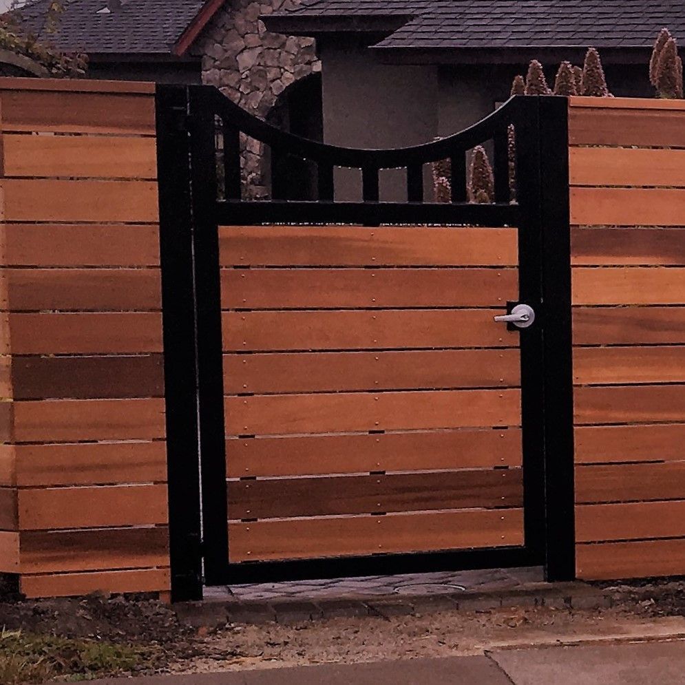 A wooden fence with a black gate in front of a house
