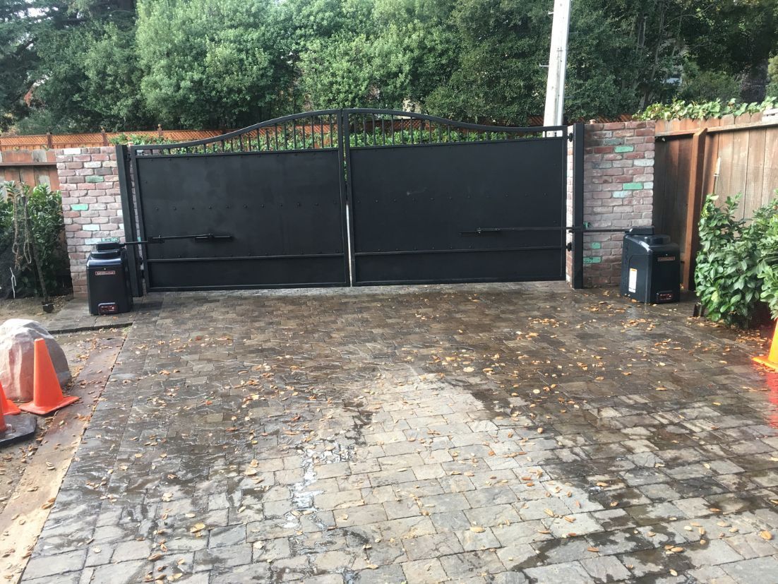 A black gate is sitting in the middle of a brick driveway.