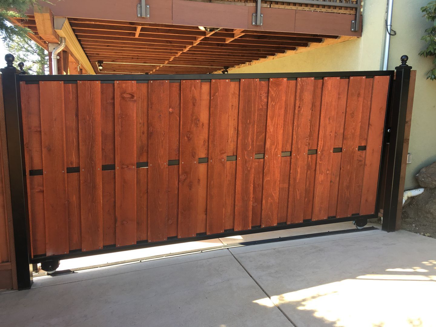 A wooden gate is sitting on a concrete driveway next to a house.