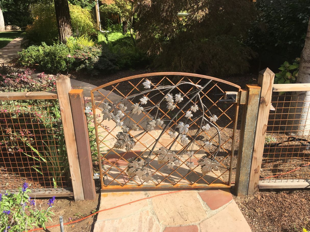 A metal gate with flowers on it is surrounded by a wooden fence.