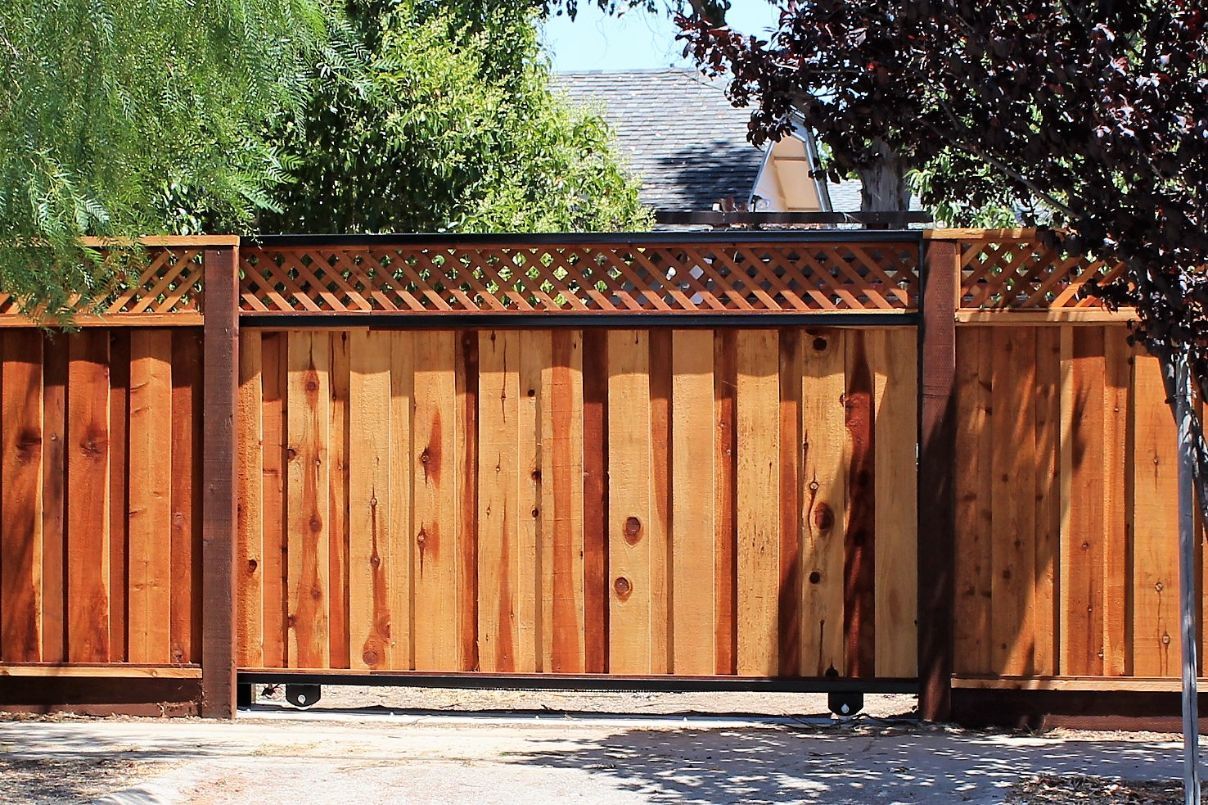 A wooden fence with a sliding gate in front of a house.