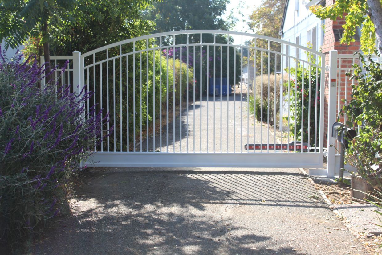 A white gate is open to a driveway in front of a house.