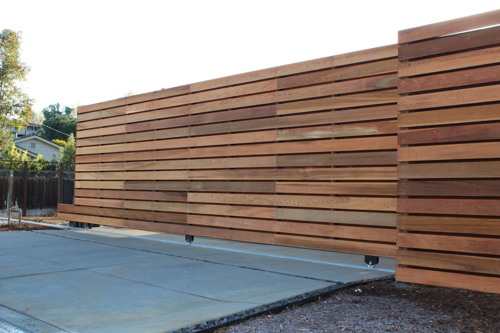 A wooden fence with a concrete driveway in front of it