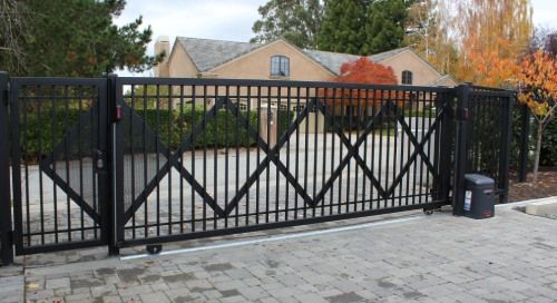 A sliding gate is open to a driveway in front of a house.