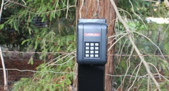 A keypad is sitting on a pole next to a tree.