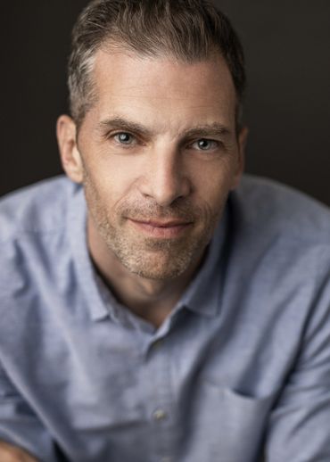Man in a blue shirt looking directly at the camera with a slight smile.