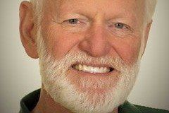 Smiling man with a white beard and short white hair, wearing a green shirt, close-up shot.