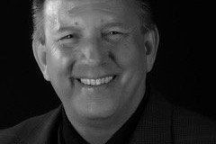 Smiling man in a dark suit against a black backdrop.