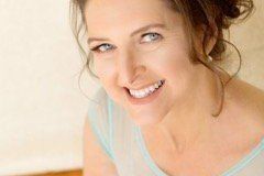 Woman with light skin, blue eyes, smiling, wearing a blue top, against a pale background.