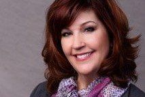 Woman with auburn hair, smiling, wearing a patterned scarf and a gray top.