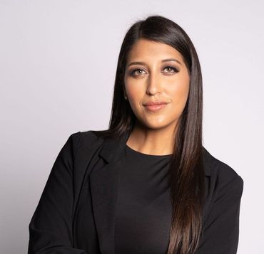 Woman in black blazer, arms crossed, looking at the camera. Neutral background.