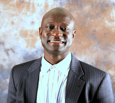 Man in pinstripe suit and white shirt smiles at the camera against a mottled background.