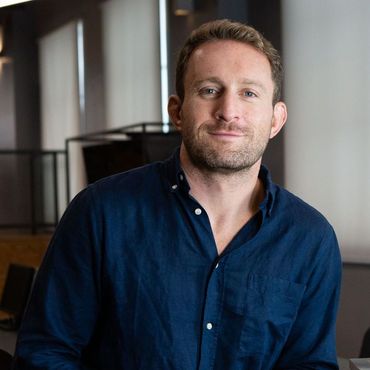 Man in a blue button-down shirt smiles, indoors.
