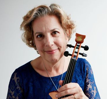 Woman holding a violin, smiling at the camera, wearing blue lace top, against a white background.