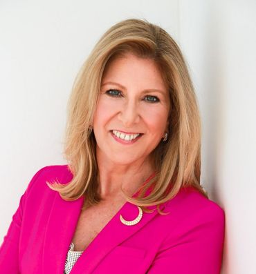Woman in a bright pink blazer smiles, leaning against a white wall.