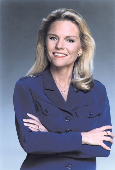 Woman with blonde hair wearing a blue blazer, arms crossed, smiling.