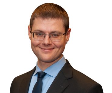 Man in glasses, smiling, wearing a suit and tie.